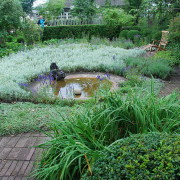 Ulla Molins trädgård. Bilden visar en damm omgiven av plattsättning och planteringar.